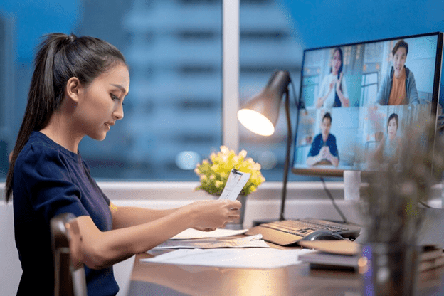 A girl reading a note standing in-front of a desktop monitor
