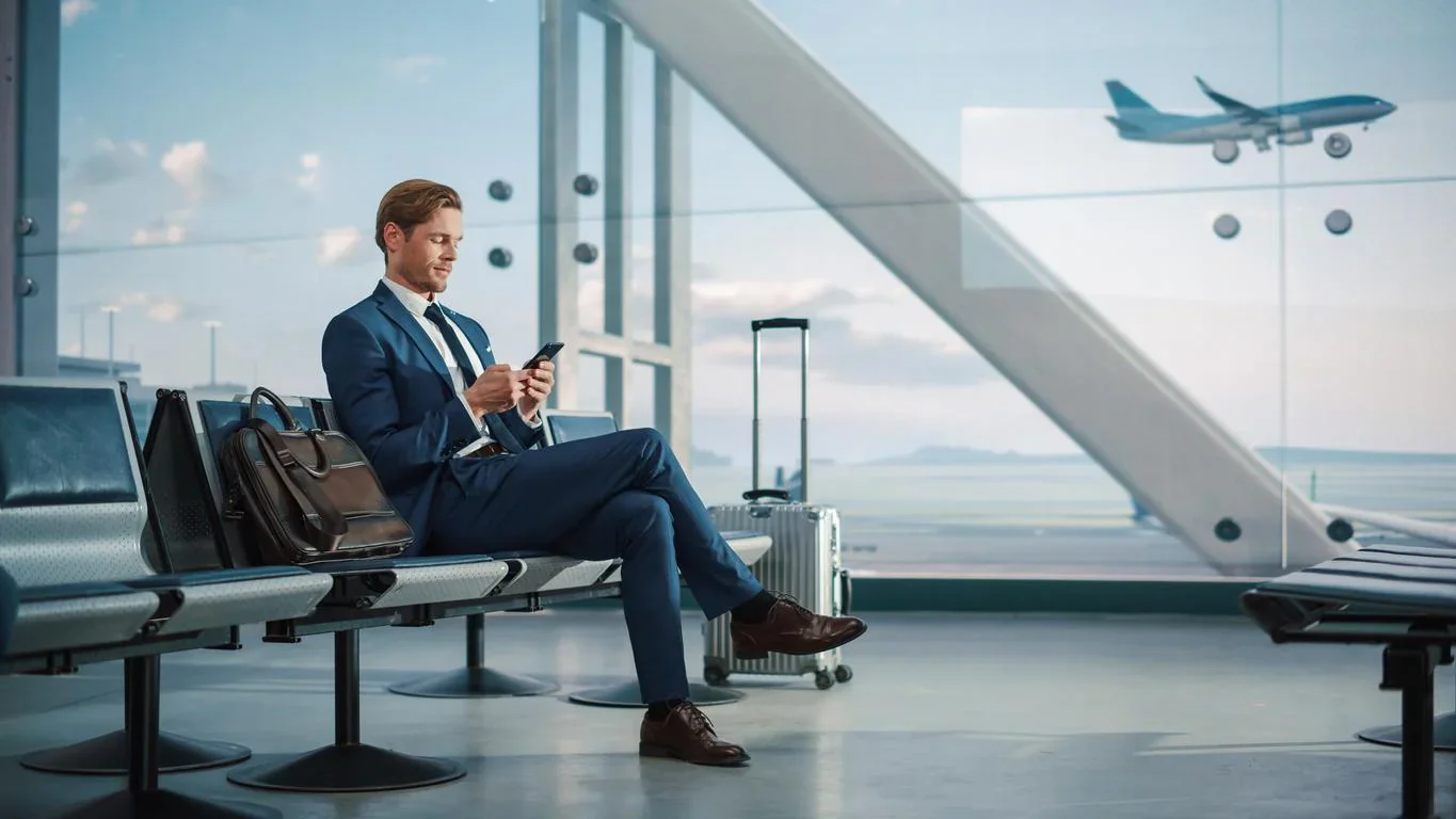 A businessman is standing with his suitcase watching an airplane