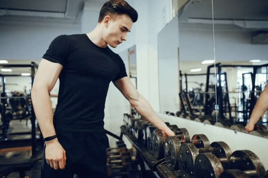 A man is holding a dumbbell at gym weight stand
